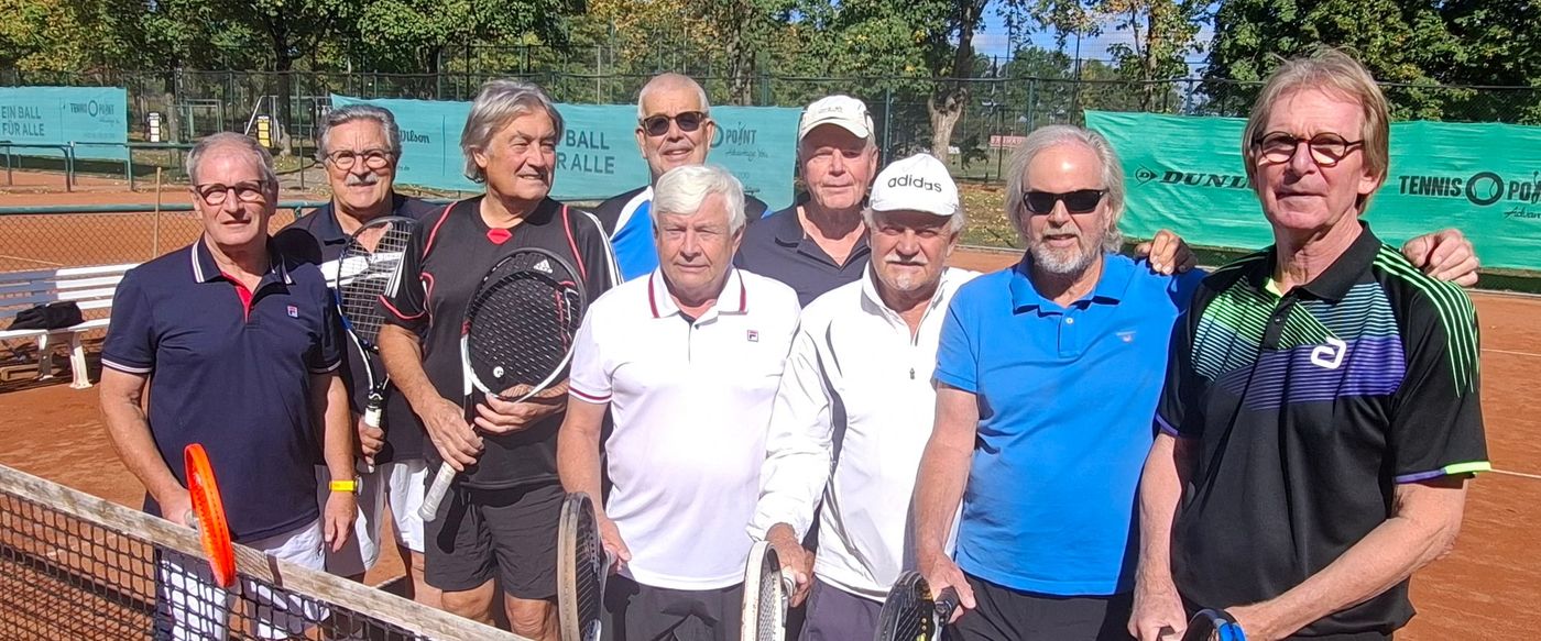 Neun Spieler der Herren 70 stehen mit ihren Schlägern am Netz auf einem Sandplatz, im Hintergrund Bäume und Banden.
