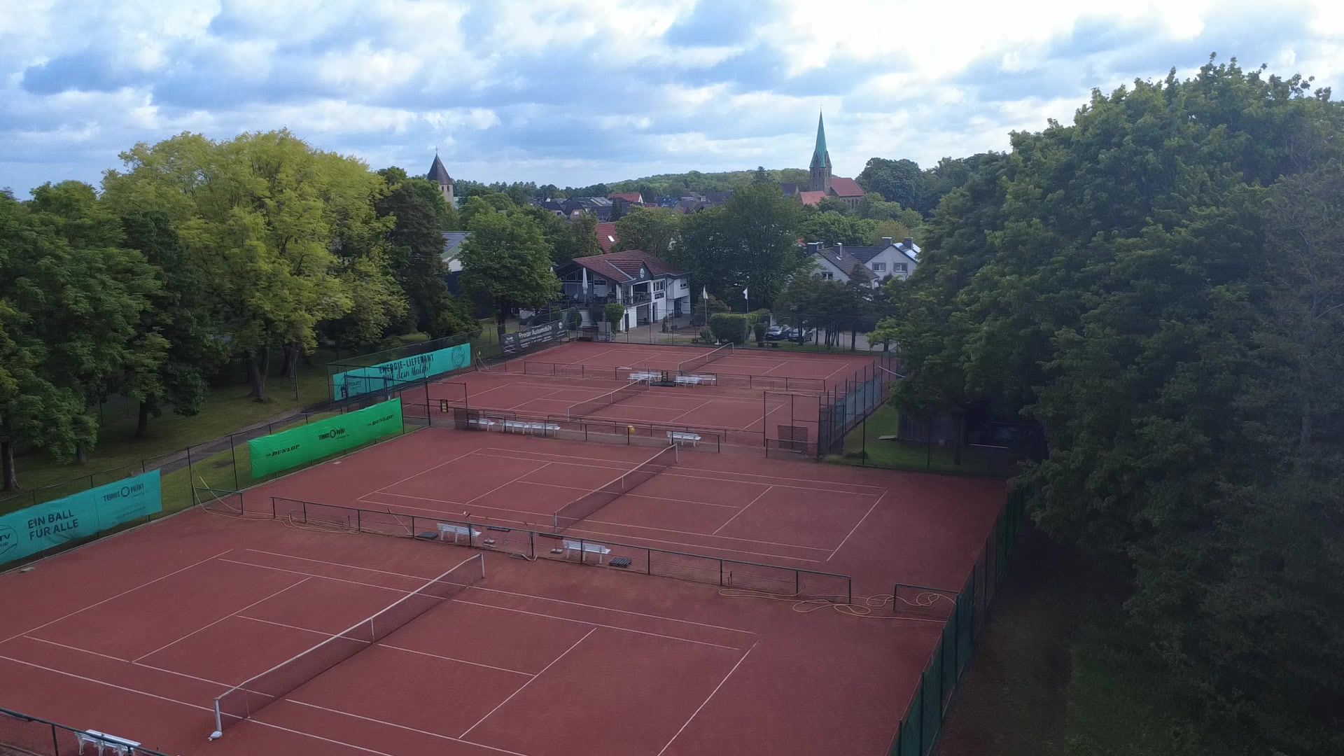Luftbild der Tennisanlage mit roten Ascheplätzen, dahinter Opherdicke mit seinem Kirchturm.