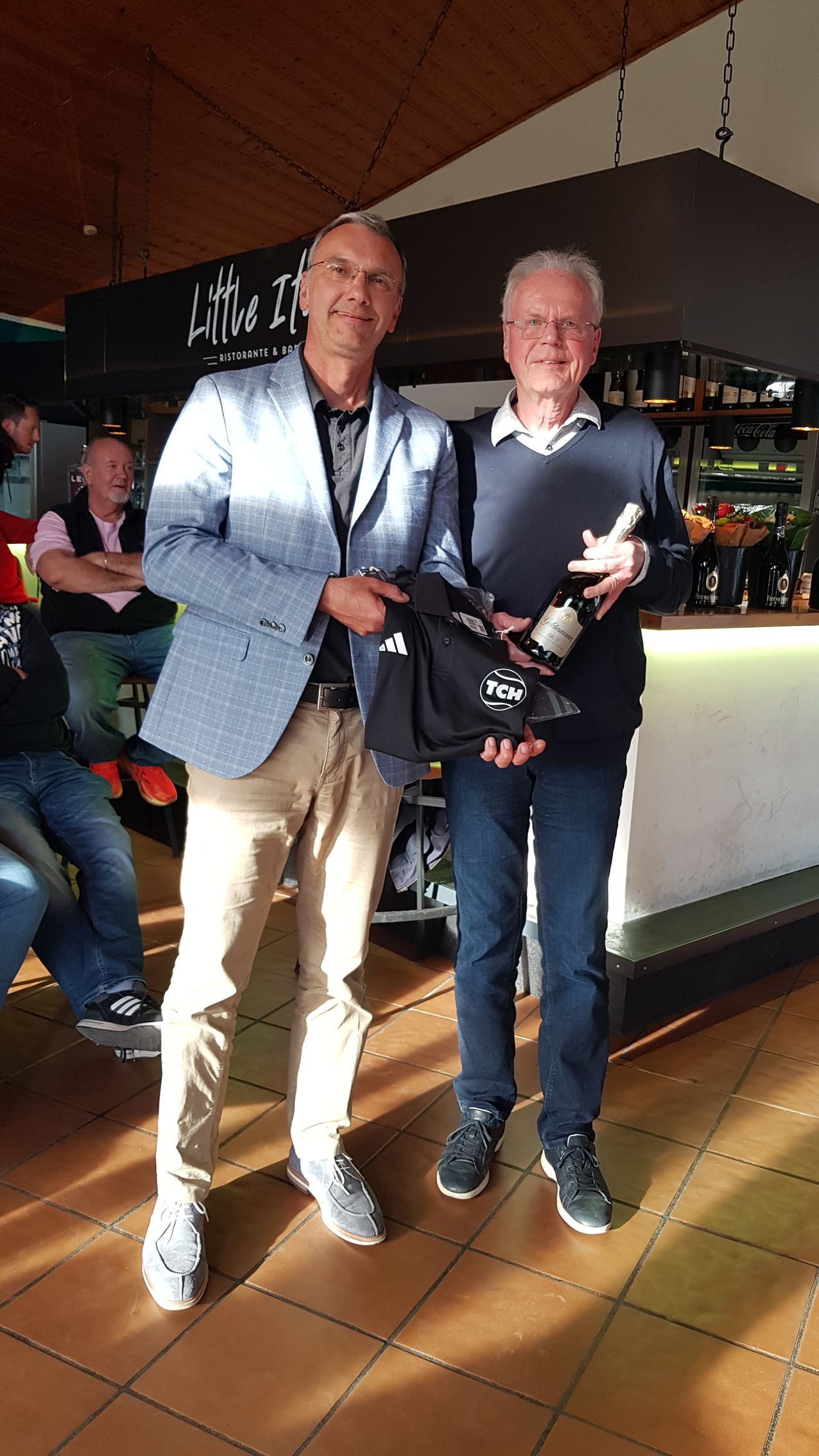Zwei Männer im Clubrestaurant, einer hält ein Geschenk.