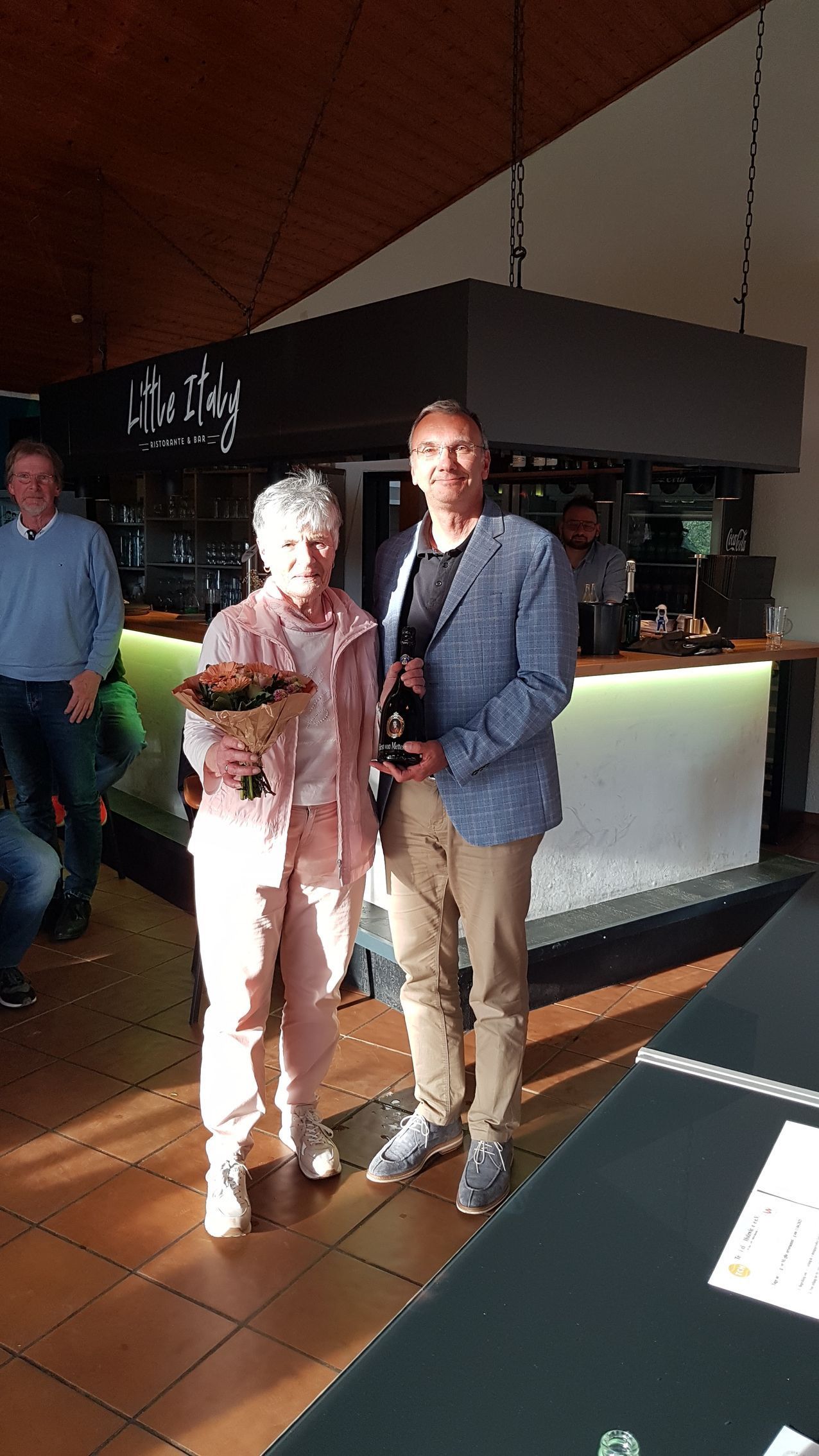 Eine Frau mit Blumenstrauß und ein Mann im Sakko im Clubrestaurant.
