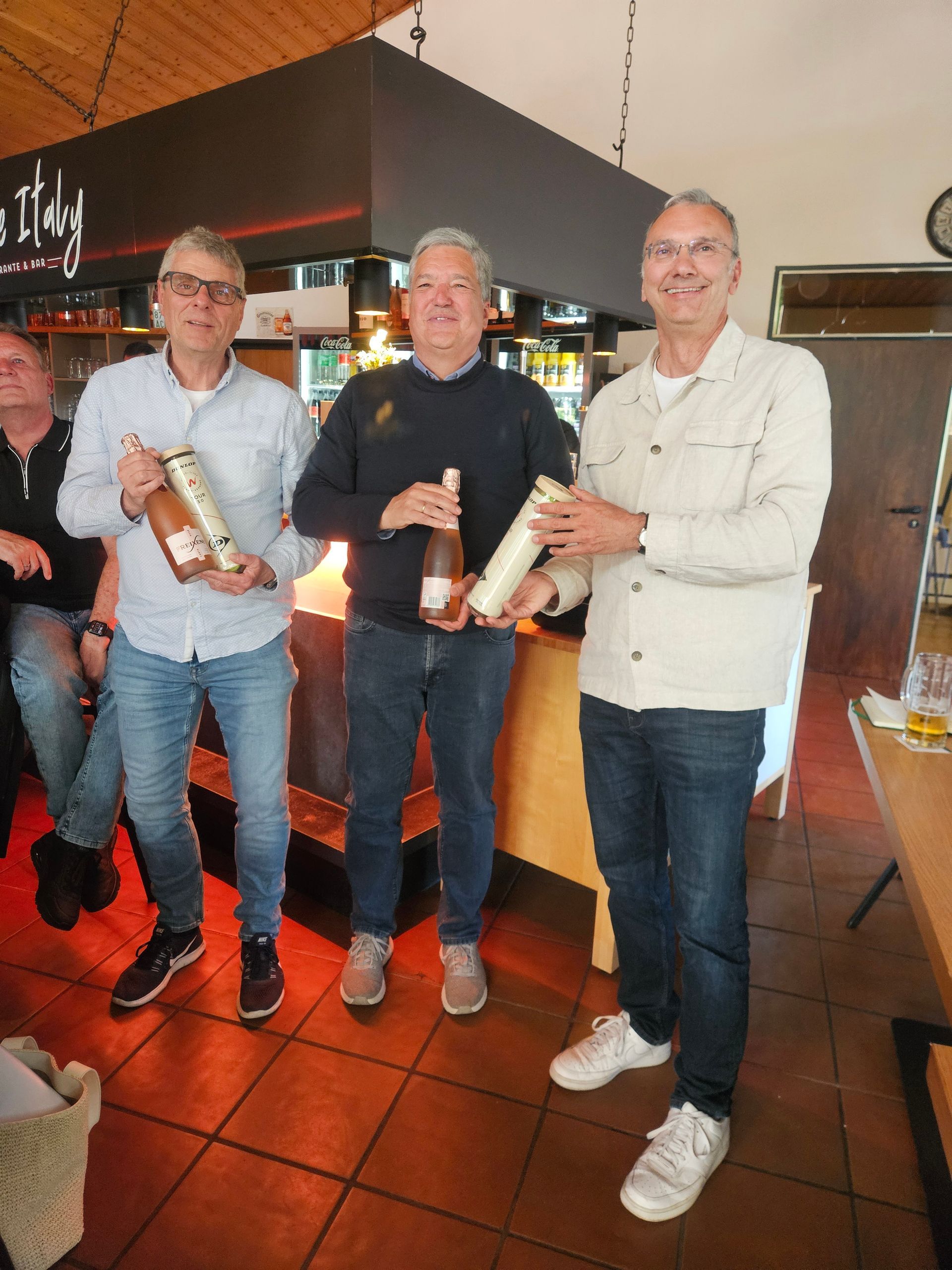 Drei Männer im Clubrestaurant, zwei halten eine Flasche als Geschenk in der Hand.